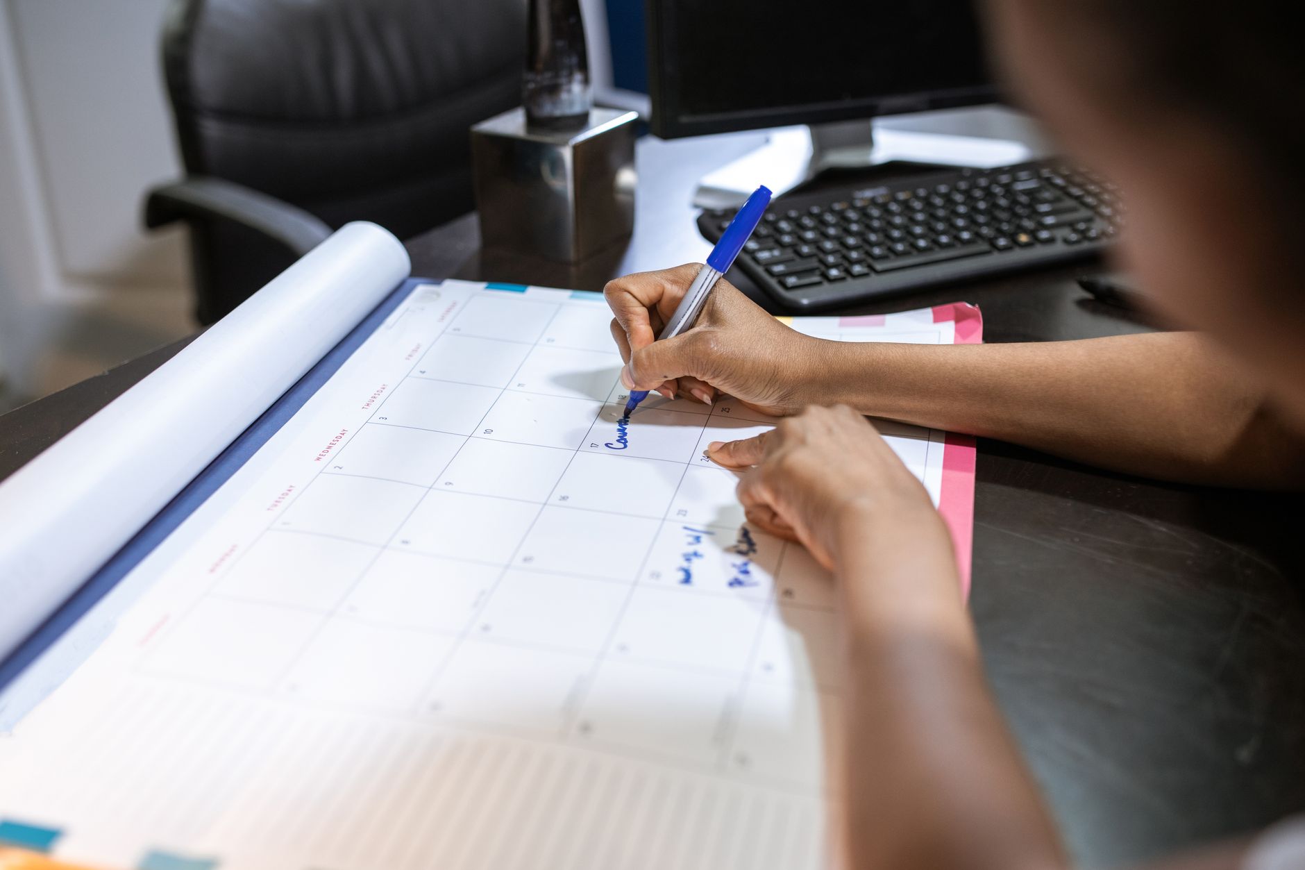 Close-up of a woman planning her schedule on a desk calendar in an office setting.