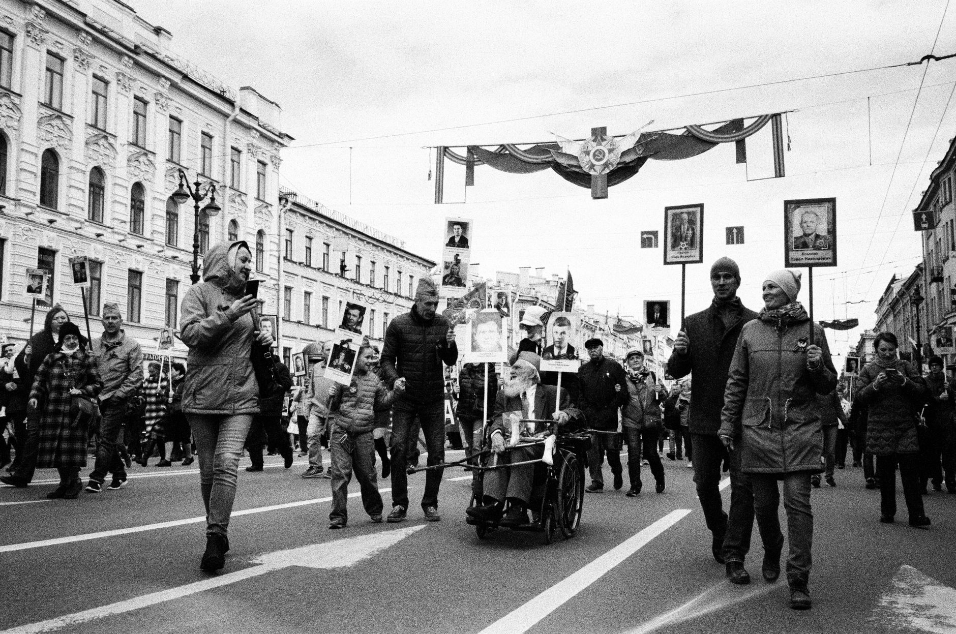 Black and white photo of a city parade scene with diverse crowds on the street.