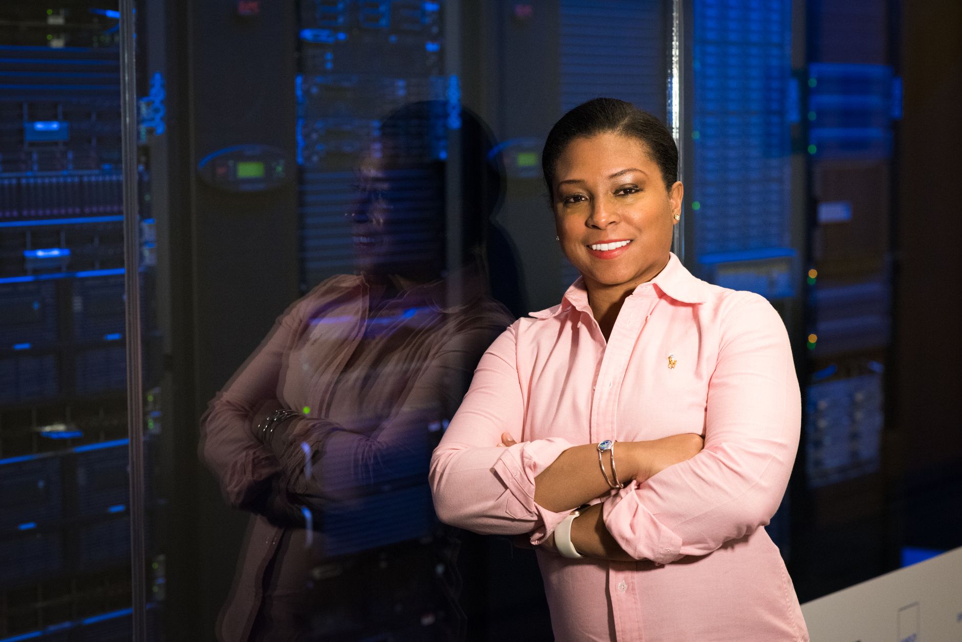 Smiling IT professional with crossed arms in a server room, reflecting her expertise.