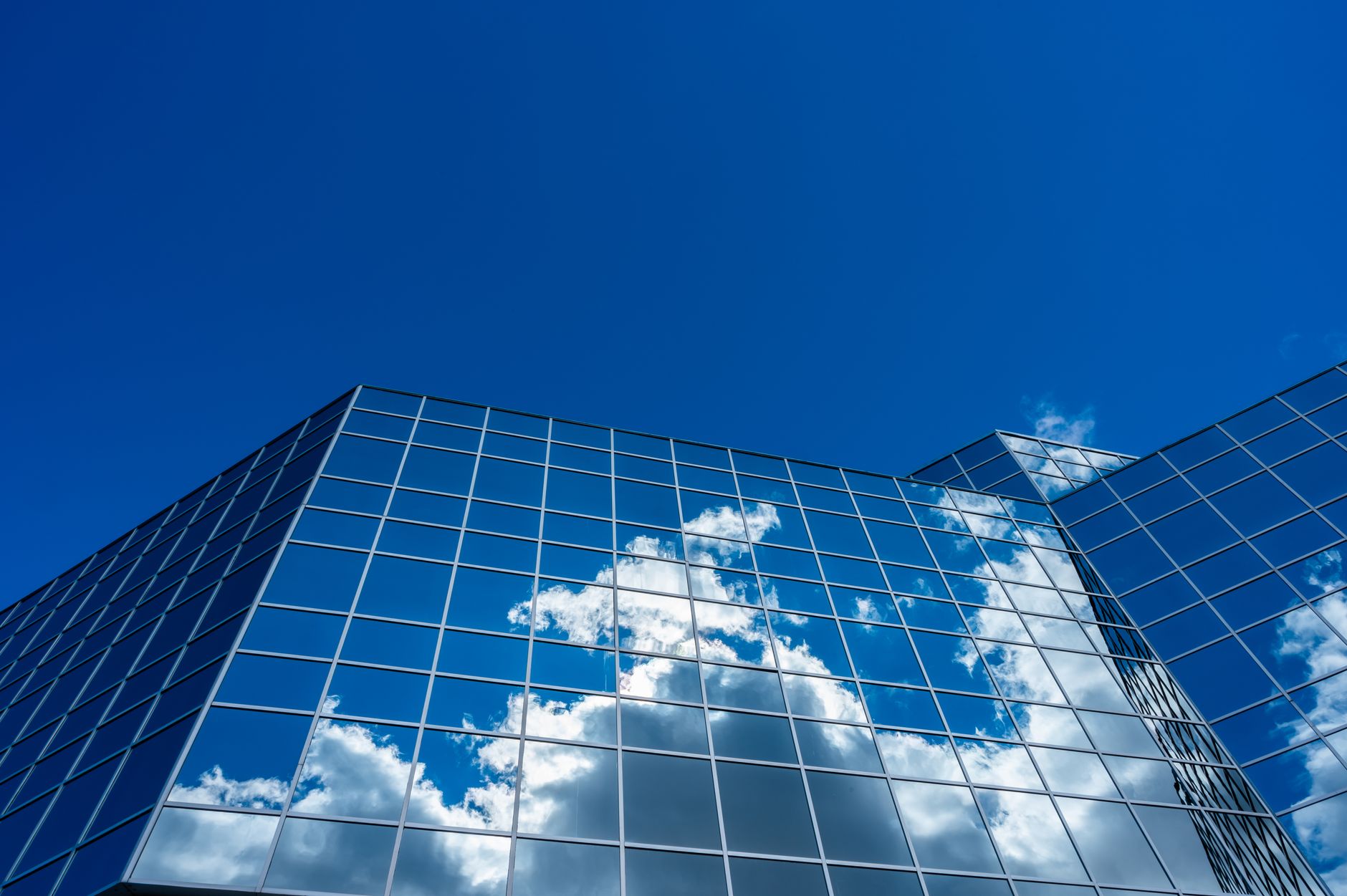 A modern skyscraper reflecting clouds against a vibrant blue sky.