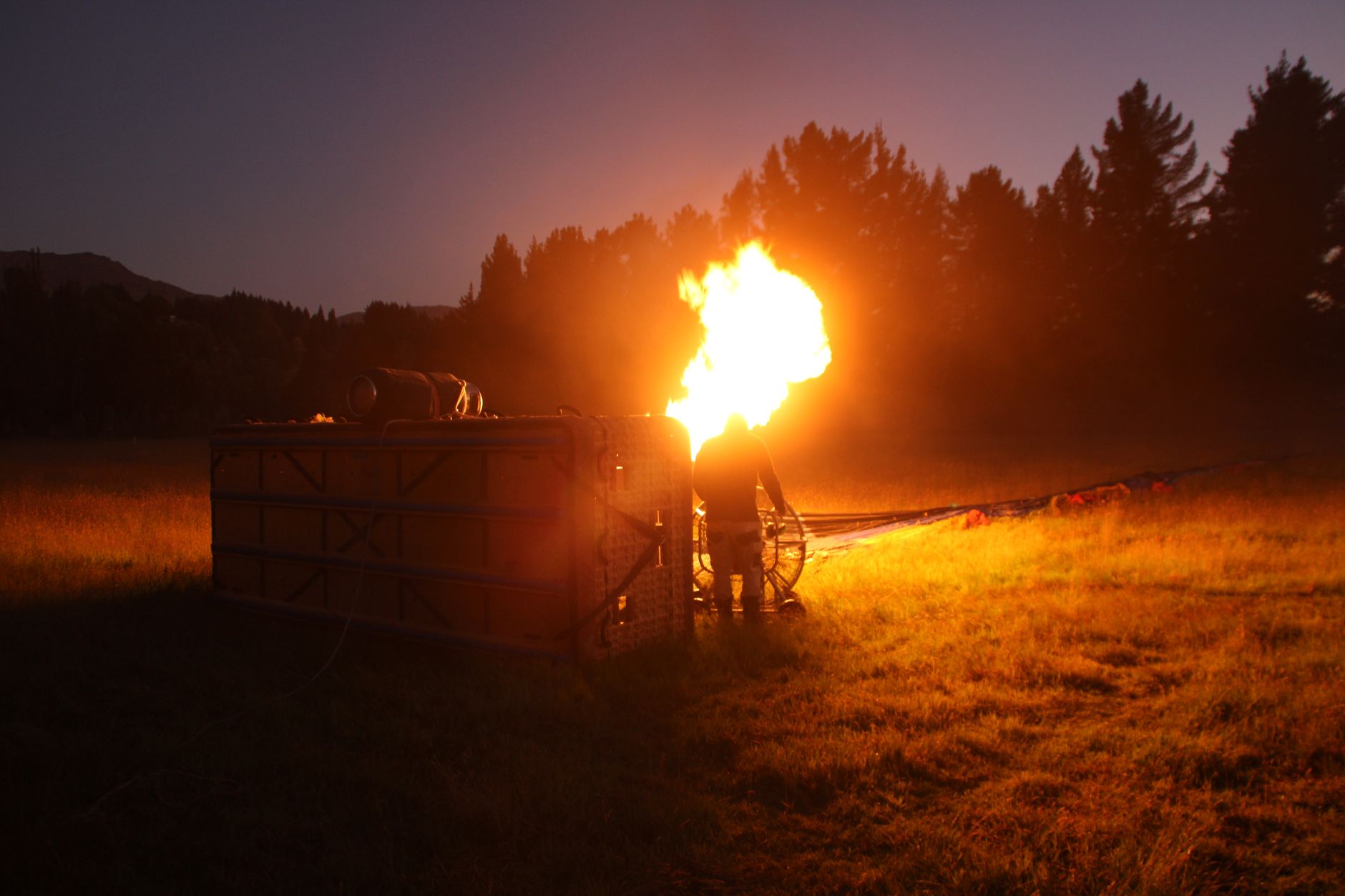 A hot air balloon being prepared with fire at dusk in a field, creating a dramatic glow.