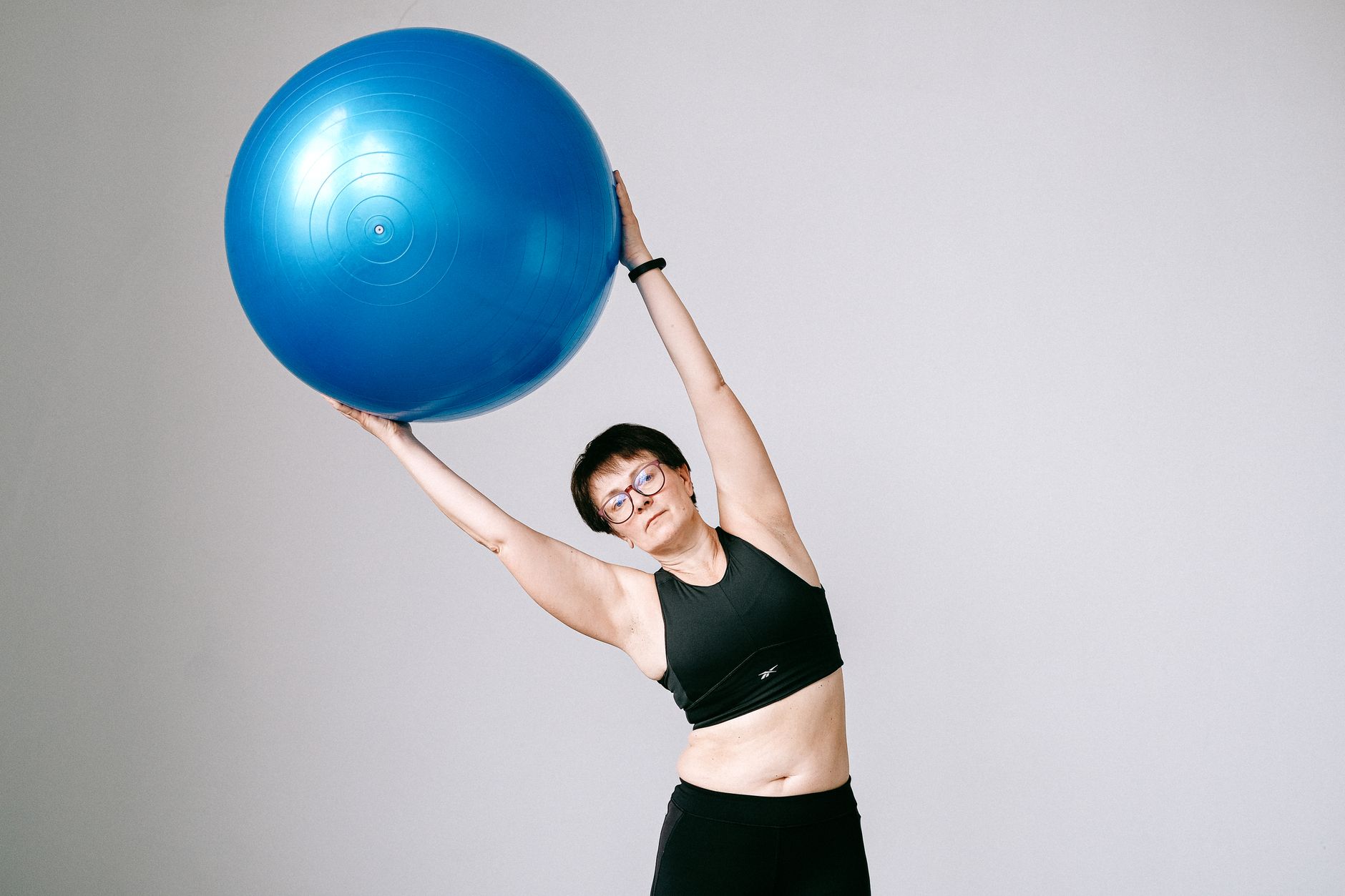 Adult woman in sportswear exercising with blue stability ball against gray background.