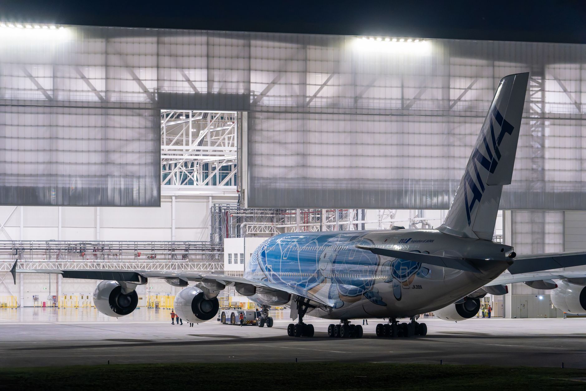 Large commercial airplane in a hangar at night with open doors showcasing the aircraft.